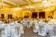 Elegant banquet hall with round tables, white chairs, floral centerpieces, and soft lighting.