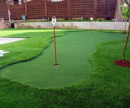 Minigolfplatz im Garten mit grünem Kunstrasen und zwei rot-weißen Fahnen.