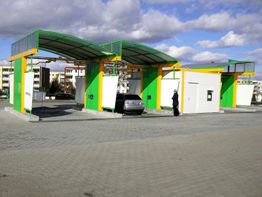 Auto in moderner grüner Waschanlage auf gepflastertem Platz unter blauem Himmel.