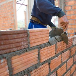 Person building brick wall with trowel and mortar.