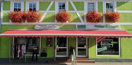 Fachwerkhaus mit grüner Fassade, Blumen und Markise, Modegeschäft im Erdgeschoss.