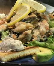 Meeresfrüchtesalat mit Zitronenscheiben, Toast, Avocado und einem Klecks Creme auf einem blauen Teller.