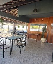 Área externa coberta com mesa e cadeiras, plantas suspensas e decoração em madeira.