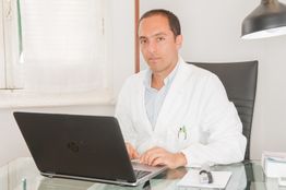 Medico in camice bianco lavora al computer in ufficio luminoso.