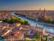 Vista aerea di Verona al tramonto, con fiume Adige e storici edifici in mattone rosso.