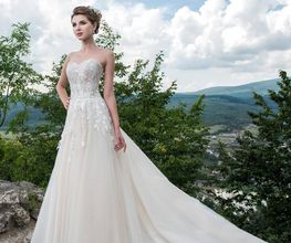 Novia en vestido blanco de encaje en paisaje montañoso con cielo azul y nubes.