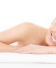 Mujer sonriente recostada sobre una toalla blanca, fondo blanco.