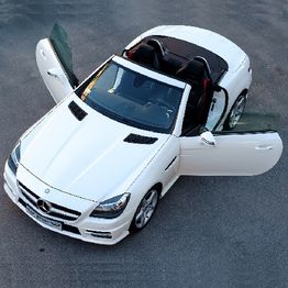 White convertible sports car with doors open, viewed from above on a gray asphalt background.