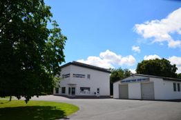 Gewerbegebäude mit Baum im Vordergrund, blauer Himmel und Wolken im Hintergrund.