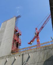 Baustelle mit großem Kran und halb errichtetem Betonbau gegen blauen Himmel.