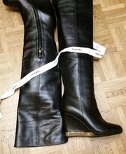 Schwarze Stiefel mit Keilabsatz auf Holzboden, mit weißem Chanel-Band verziert.