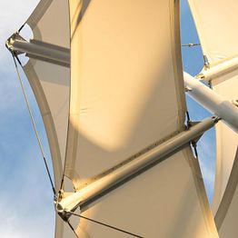 Close-up of white sails against a blue sky, with sunlight casting shadows on the fabric.