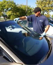 Mann wechselt die Windschutzscheibe eines Autos im Freien bei sonnigem Wetter.