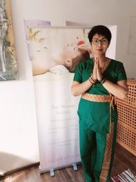 Person in traditioneller Kleidung vor einem Banner mit dem Text "Thai Massage NANG".