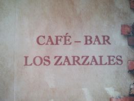 Texto en la pared: "Café - Bar Los Zarzales" en fondo de ladrillos.