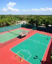 Cancha de fútbol y tenis al aire libre con árboles alrededor y cielo despejado.