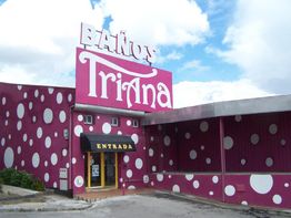 Edificio rosa con puntos blancos y letrero "Baños Triana". Entrada con cielo parcialmente nublado.