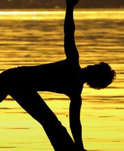 Ein Mensch macht eine Yoga-Pose am Strand bei Sonnenuntergang.