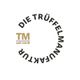 Logo: „Die Trüffelmanufaktur“ in einem Kreis, daneben „TM seit 2008“ in Gold.