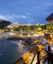 Vista nocturna de una playa con restaurantes iluminados y mesas decoradas junto al mar.