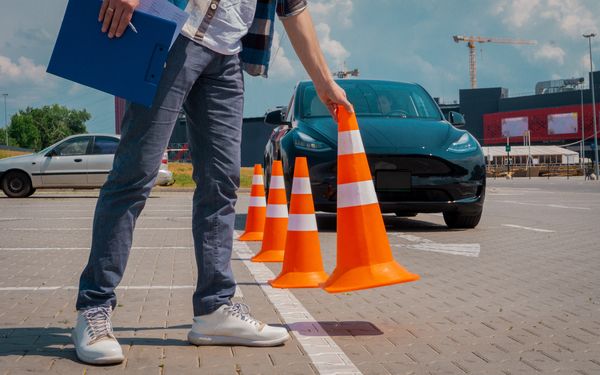 Mann stellt orange farbene Hütchen vor einem schwarzen Auto auf