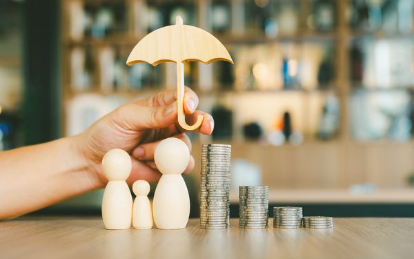 Hand hält schützend einen Regenschirm über Figuren