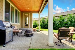 Covered patio with outdoor furniture, grill, and fire pit, overlooking a lush green backyard.