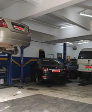 Oficina mecânica com carro levantado em elevador e outros veículos ao fundo.