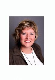 Eine lächelnde Frau mit kurzen, blonden Haaren vor grauem Hintergrund.