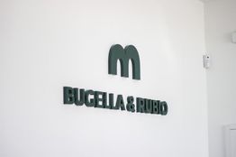 Texto en pared blanca: "BUGELLA & RUBIO" con un logotipo verde arriba.