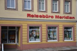 Fassade eines Reisebüros mit der Aufschrift "Reisebüro Meridian" und bunten Schaufenstern.