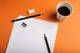 Papier, Stifte, Radiergummi, Spitzer und Kaffee auf orangefarbenem Hintergrund.