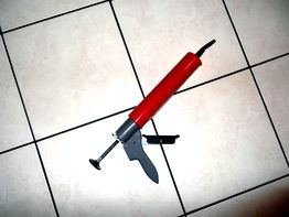 Rote Kartuschenpresse auf weiß gefliesten Boden, schräg nach oben gerichtet.