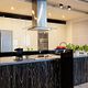 Modern kitchen with island, stainless steel hood, and plants on the counter.