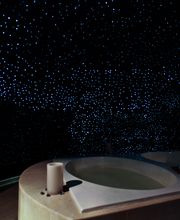 Baño con jacuzzi bajo techo estrellado. Decoración relajante y ambiente nocturno.