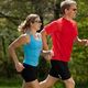 Two people jogging outdoors with trees in the background.