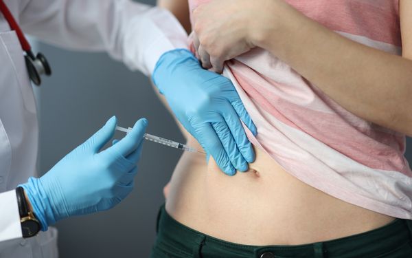 Ärztliche Person setzt einer Patientin eine Spritze in den Bauch.