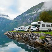 Campervans parked by a serene lake with majestic mountains in the background.