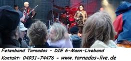 Liveband spielt auf Bühne; Zuschauer im Vordergrund. Text: Kontaktinfos und Website der Band.