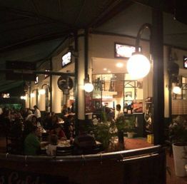 Restaurante movimentado à noite com pessoas jantando em várias mesas iluminadas.