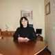 Donna seduta a un tavolo di legno in ufficio, con un computer sullo sfondo.