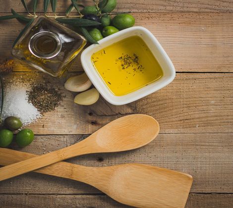 Olio d'oliva, spezie, aglio e cucchiai di legno su tavola rustica di legno.