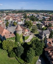 Luftaufnahme einer Stadtlandschaft mit vielen Häusern, einem Turm und grünen Bäumen.