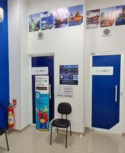 Sala de espera com paredes e portas azuis, cadeiras pretas e fotos de paisagens na parede superior.