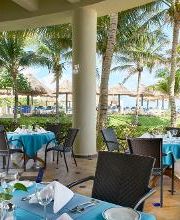 Restaurante al aire libre frente al mar con mesas cubiertas de manteles azules y sillas negras.