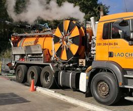 Oranger LKW mit Technik-Aufbau und Schlauch an einem Straßenrand, in Betrieb mit Dampfentwicklung.