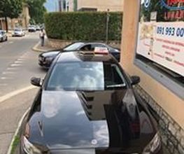 Schwarzes Auto geparkt auf einer Straße, Gebäude und Berge im Hintergrund.