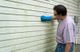 Man cleaning house siding with a sponge while wearing blue gloves.