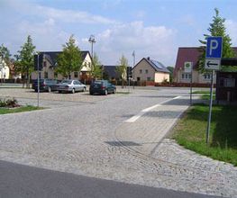 Parkplatz mit Kopfsteinpflaster, ein paar Autos, Häuser im Hintergrund, blaues "P"-Schild.