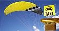 Gelbes Paraglider mit Taxi-Schild im Hintergrund und blauem Himmel.